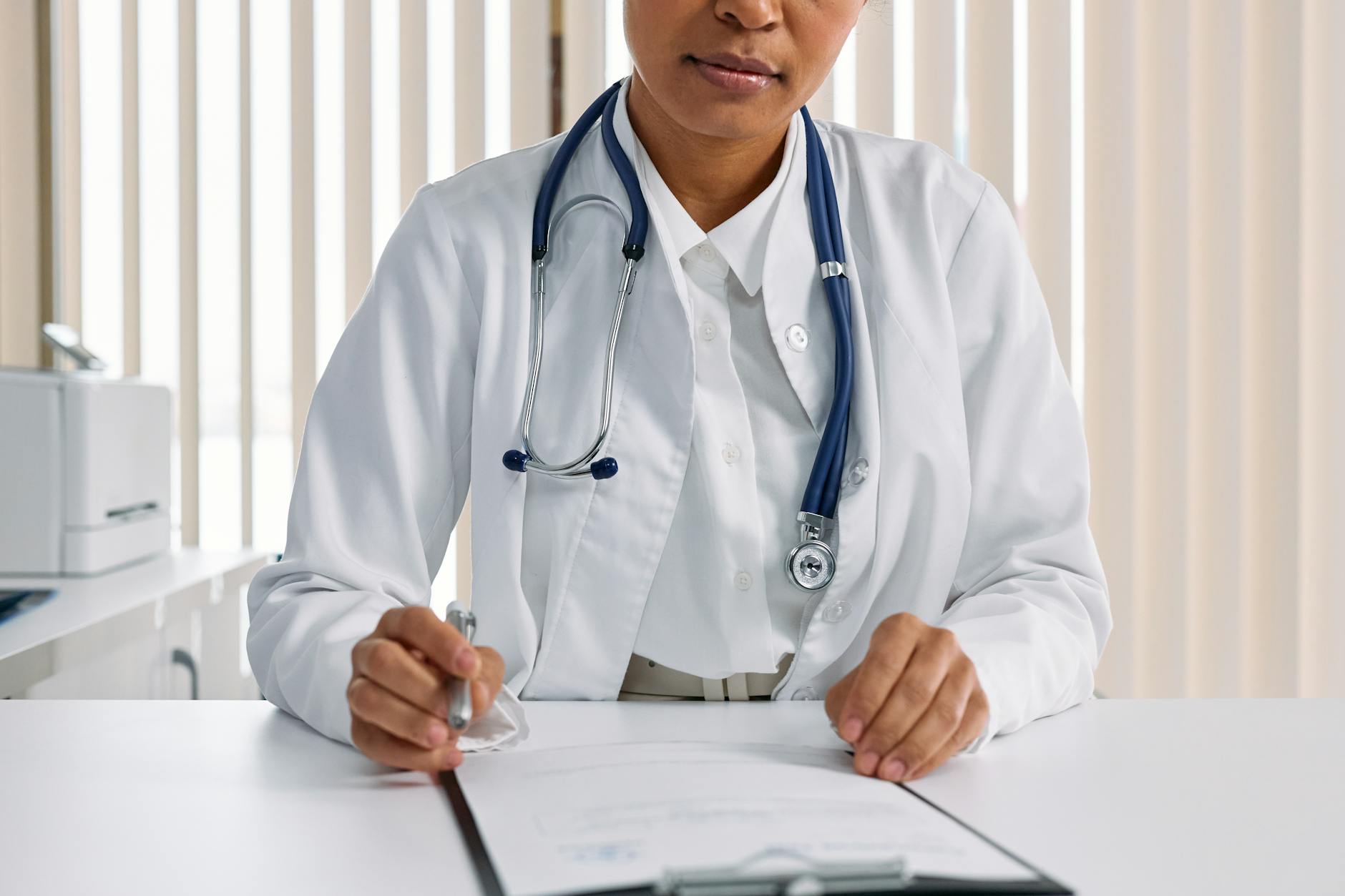 A focused doctor with stethoscope recording patient details in an office setting.