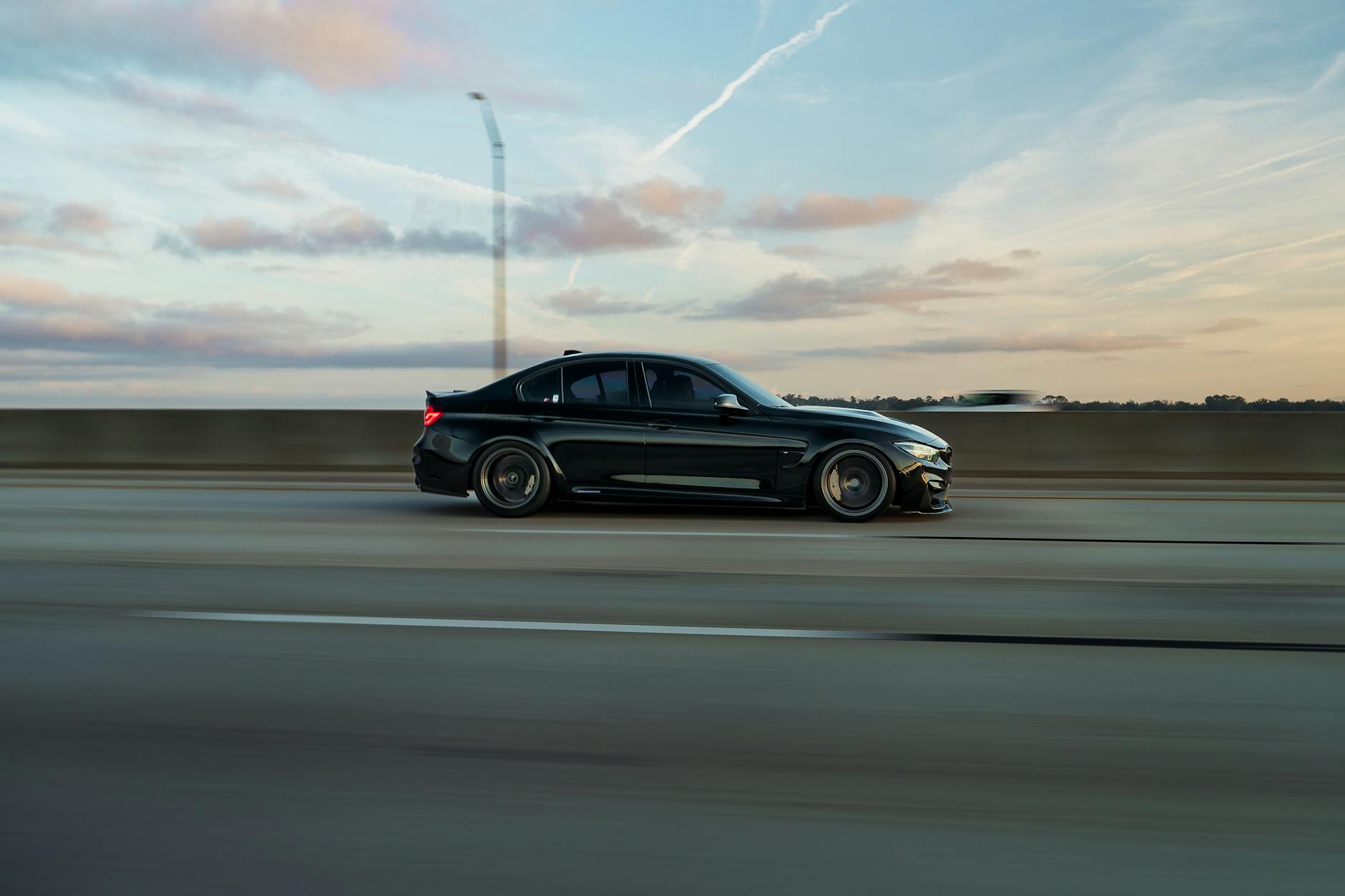 Black sedan speeding down highway at sunset, showcasing motion and luxury.