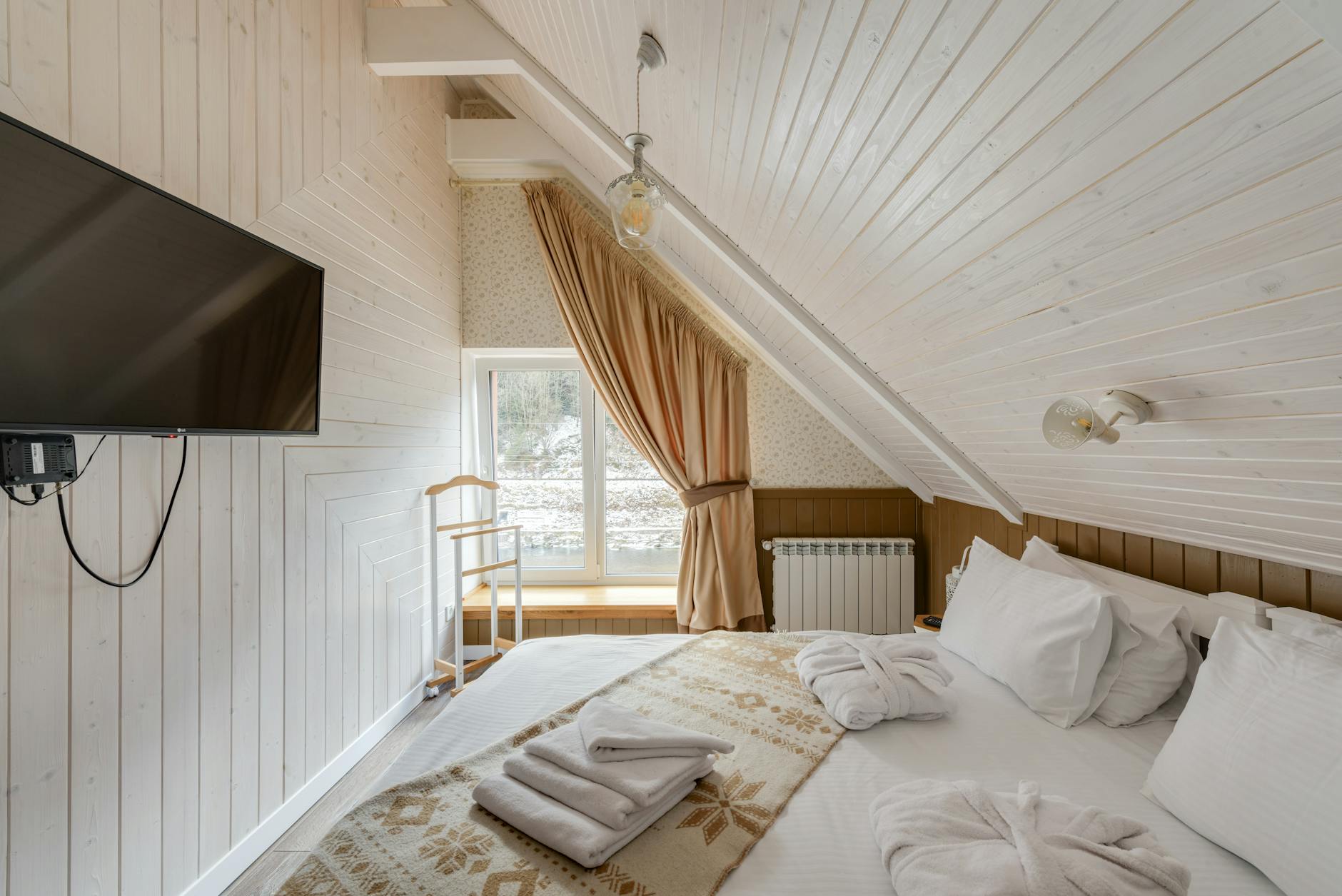 Inviting attic bedroom featuring modern design, wooden paneling, and TV.