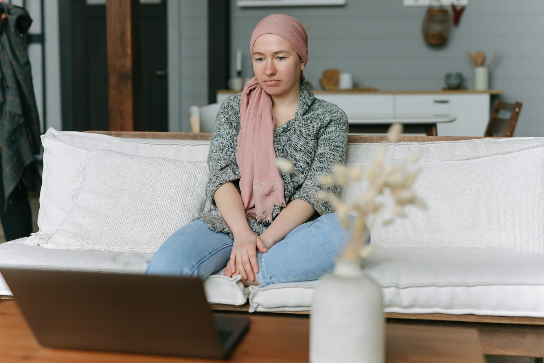 Woman with head cover sits on a sofa, using a laptop, conveying focus and introspection.