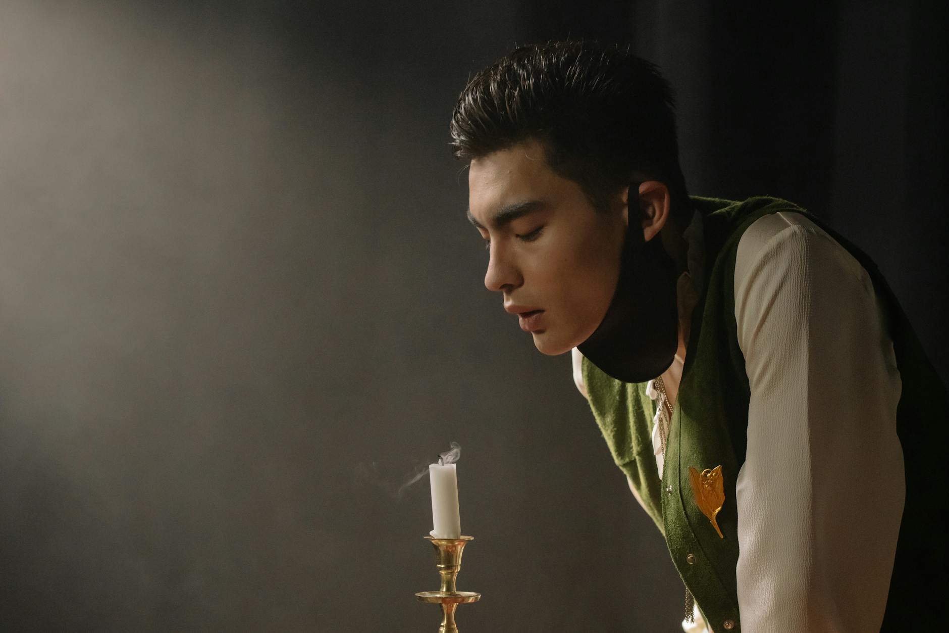 A man in a dark setting blowing out a candle, with visible smoke curling upwards.