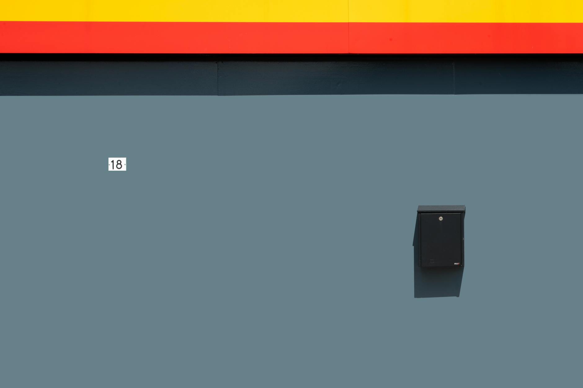 Captivating minimalist wall with a mailbox and number 18, featuring bold color contrasts.