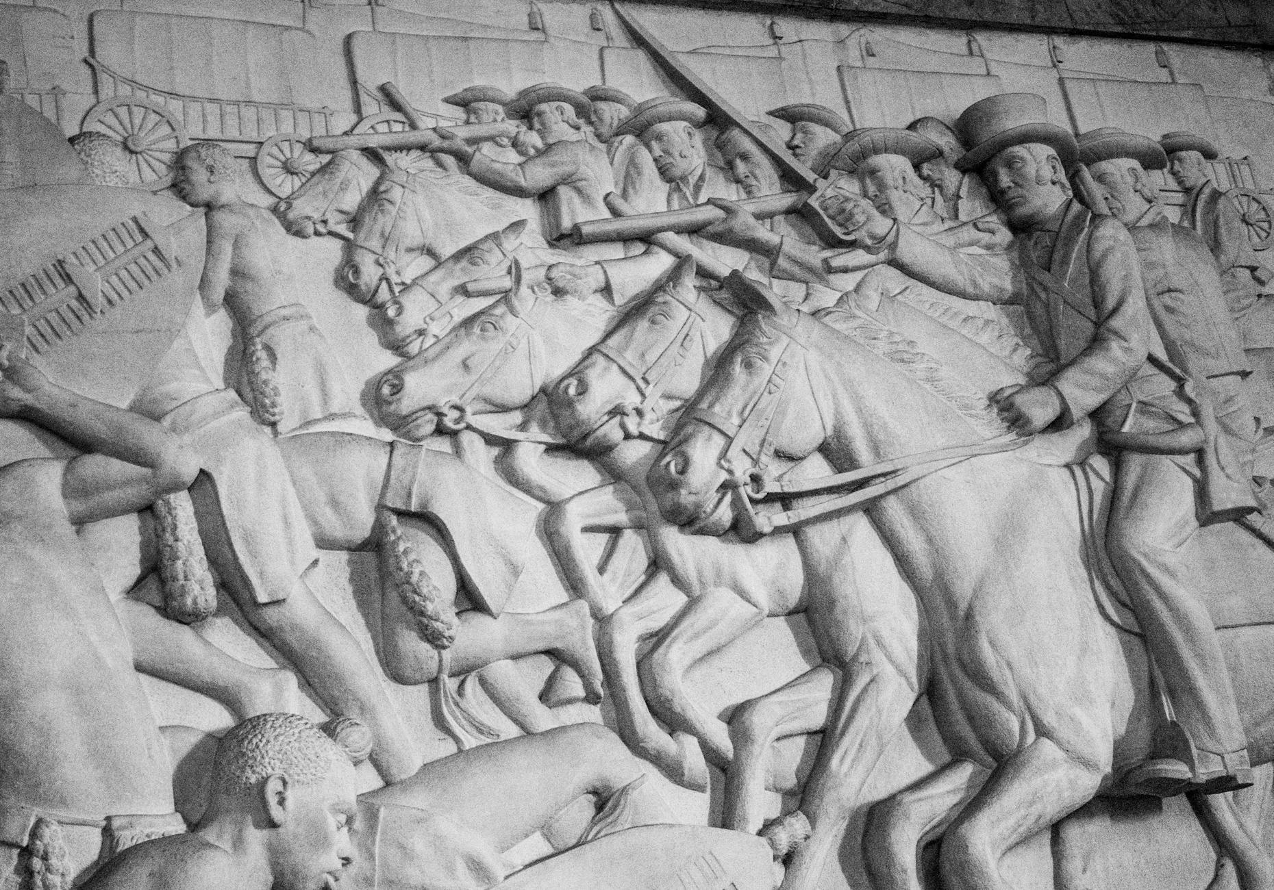 Detailed black and white bas relief depicting a historic cavalry charge with soldiers and horses.