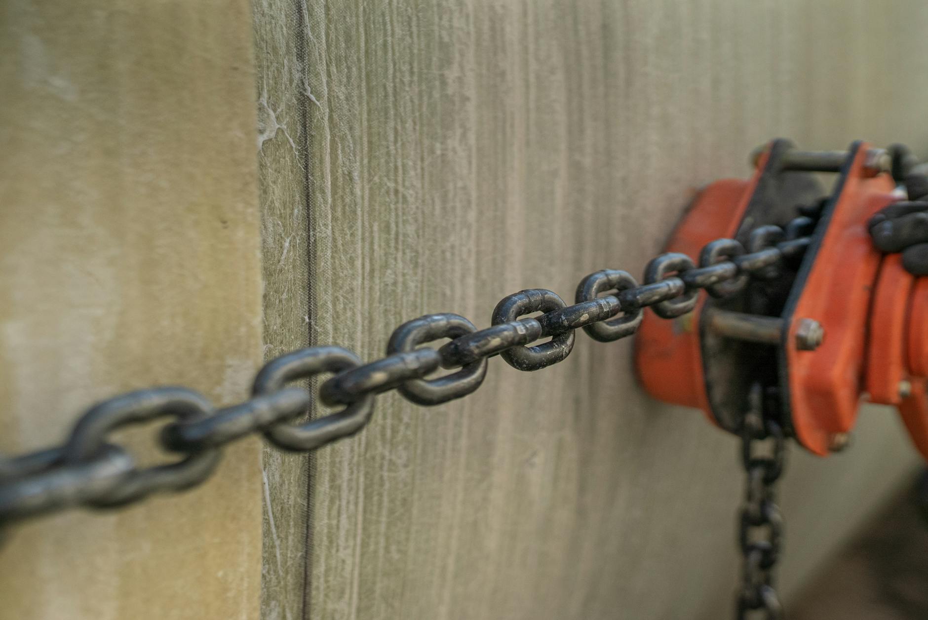 Detailed view of a metal chain connected to an orange pulley on a textured surface.